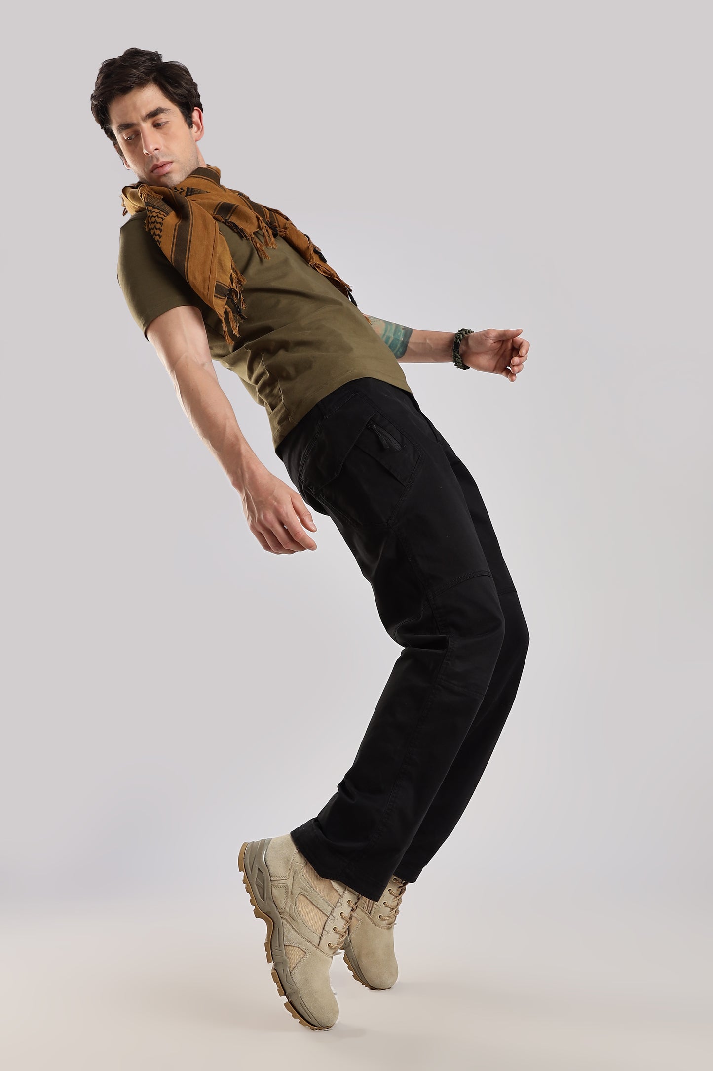 Man in brown tactical shemagh, olive green tshirt, black cargo pants and desert combat boots posing against a white background.