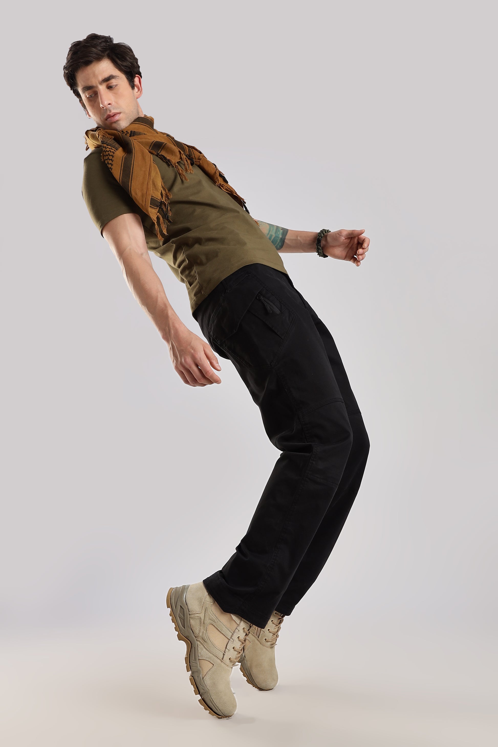Man in brown tactical shemagh, olive green tshirt, black cargo pants and desert combat boots posing against a white background.