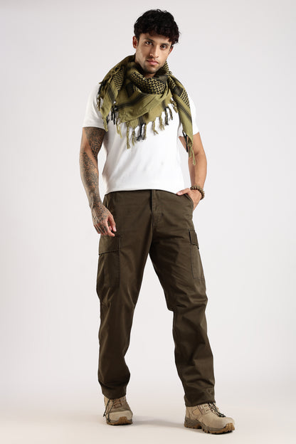 Man wearing an olive green tactical shemagh scarf, a white t-shirt and green cargo pants on a white background.