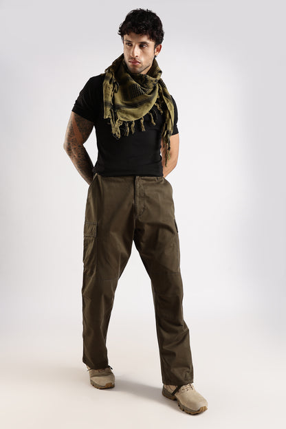 Man wearing an olive green tactical shemagh scarf in digital camo pattern, a black t-shirt and olive green paratrooper fatigue cargo on a white background